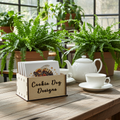 Bee design coaster set in a wooden box labelled 'Cookie Dog Designs' on a wooden table with plants in the background.