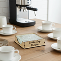 Wooden box containing glass coasters with 'Cookie Dog Designs' branding on a table with coffee cups and an espresso machine.