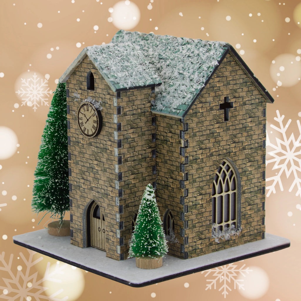 Model of a stone church with snow on the roof, surrounded by Christmas trees on a decorative background.