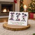 Christmas card with cartoon dogs on a wooden stand in a festive setting with a fireplace and tree.