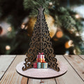 Decorative wooden Christmas tree with small gift boxes on a wooden platform against a blurred Christmas tree background.