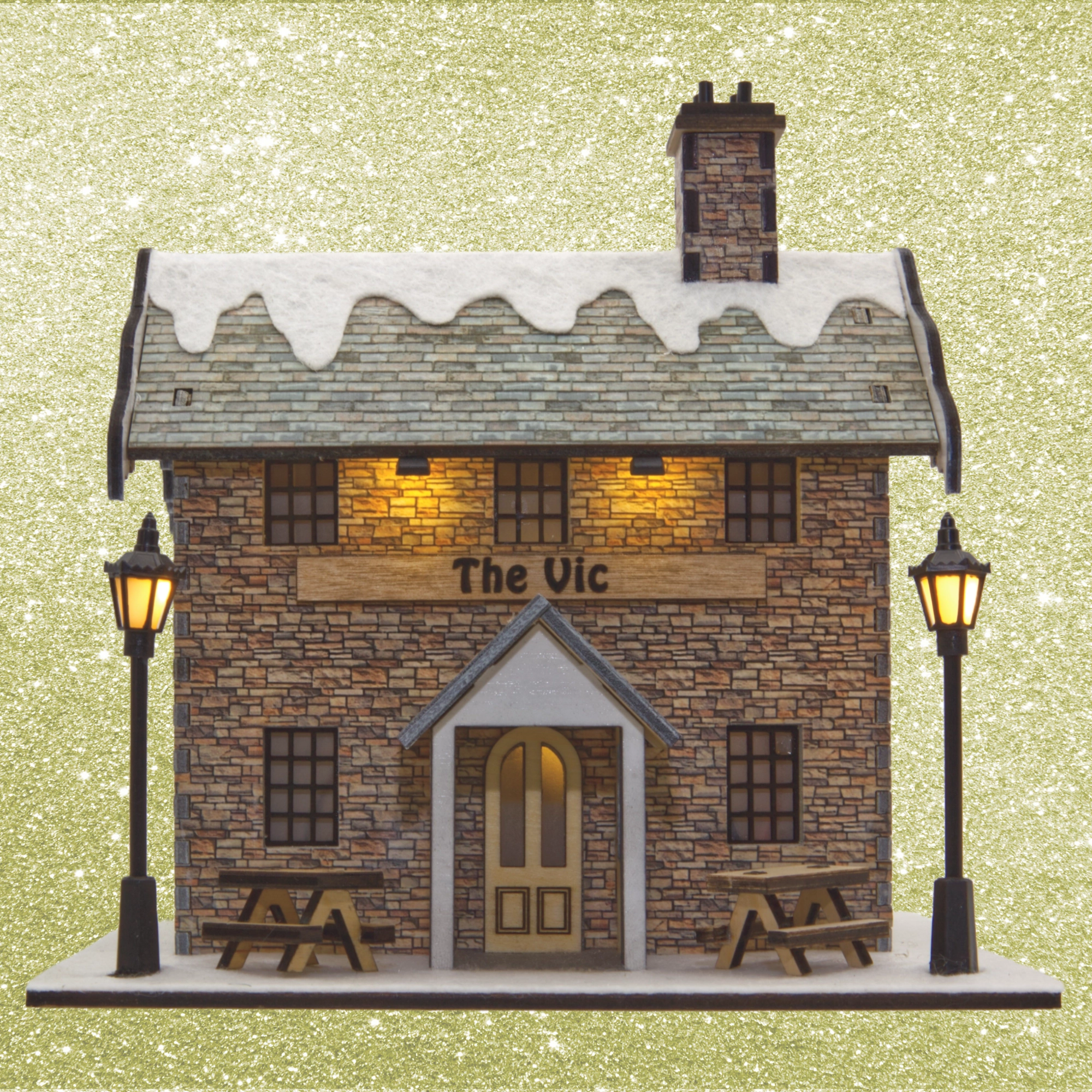 Model of a pub named 'The Vic' with snow on the roof, surrounded by lampposts on a glittery gold background.