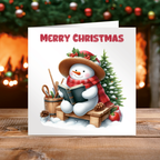 Christmas card with a snowman reading a book, surrounded by Christmas decorations.